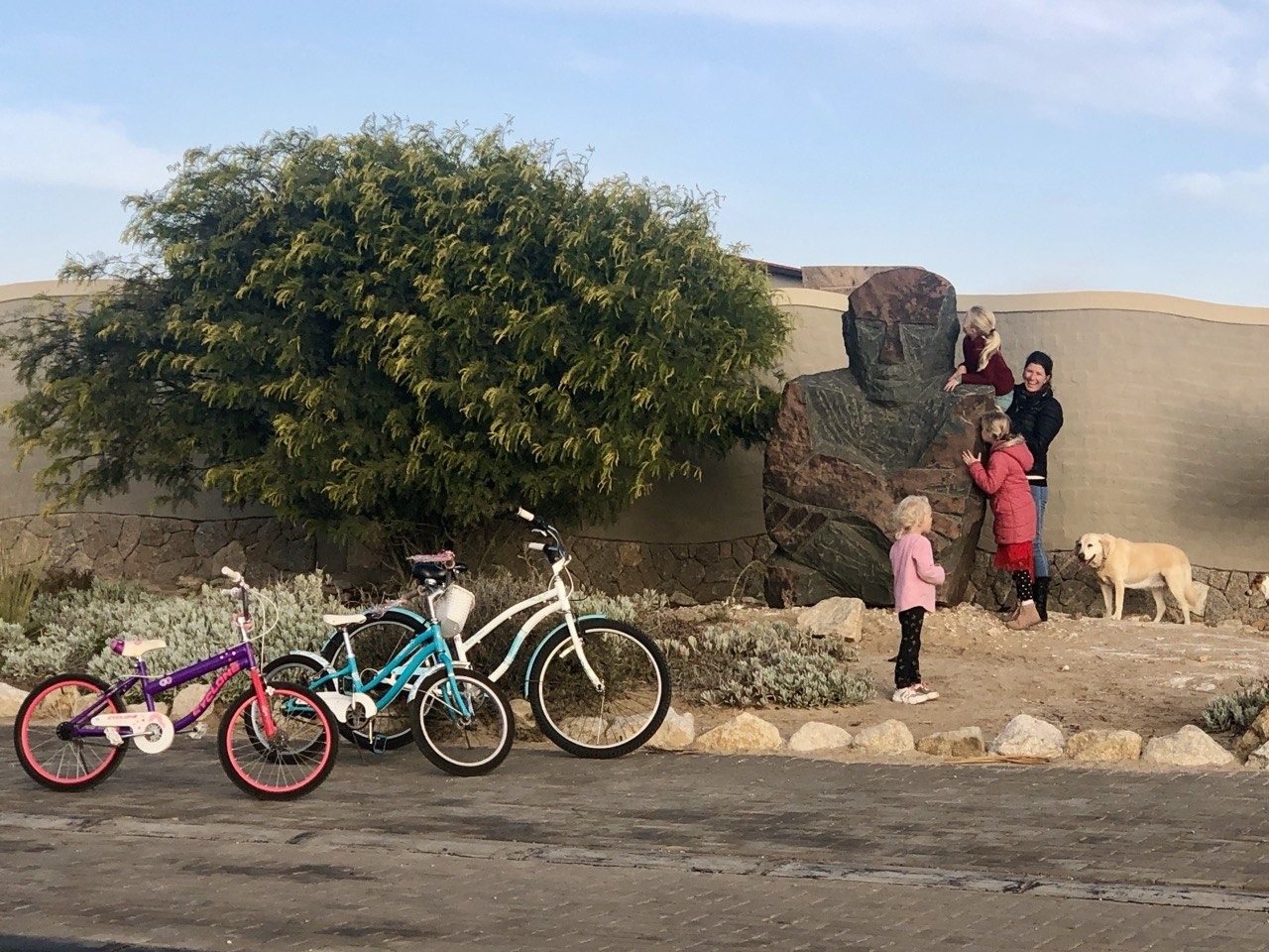 Visitors beside a stone sculpture with bicycles in the Desert Breeze garden